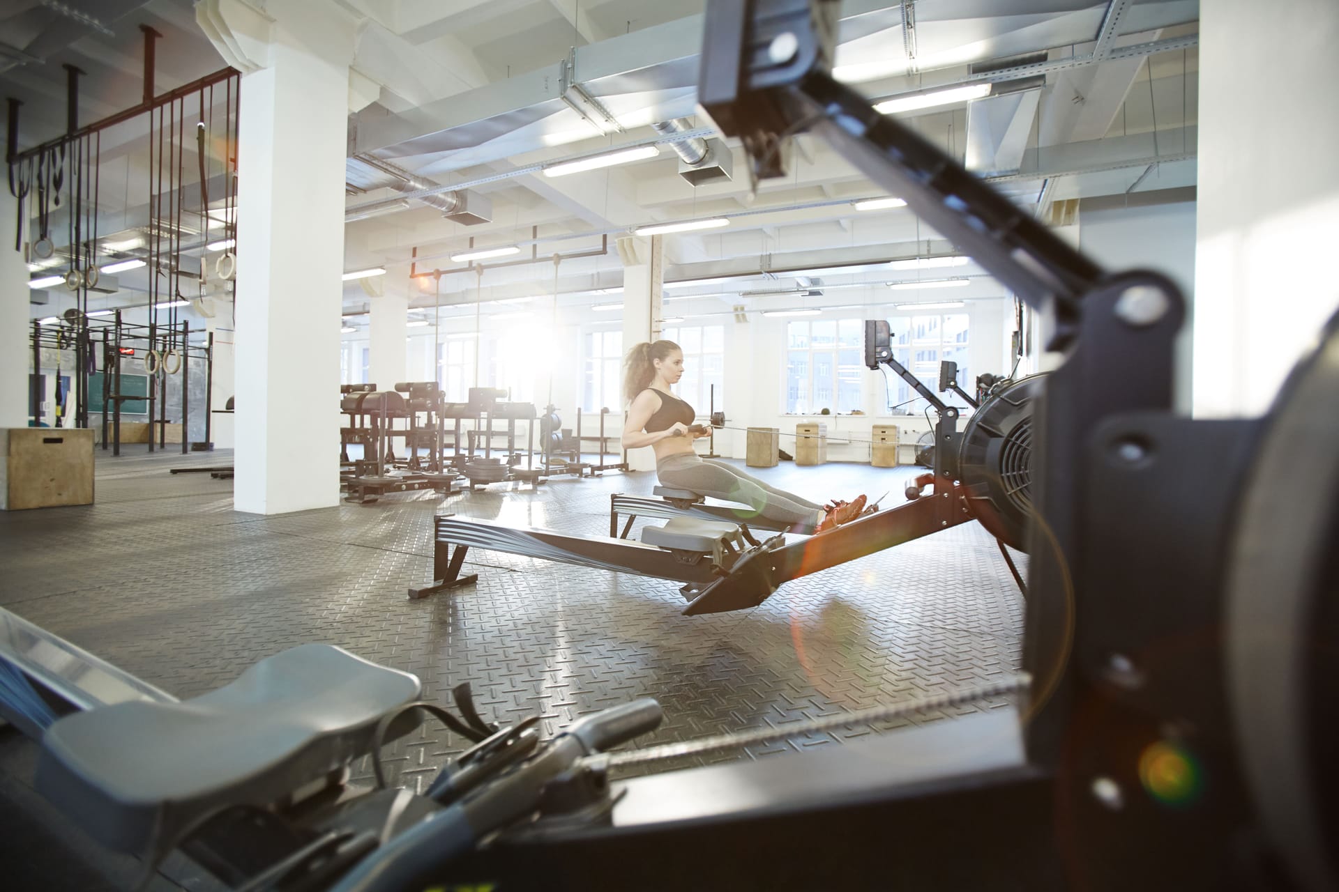 A woman at the finish position of a rowing stroke on an indoor rowing machine, legs extended and arms drawn in to the body, showing the whole-body movement