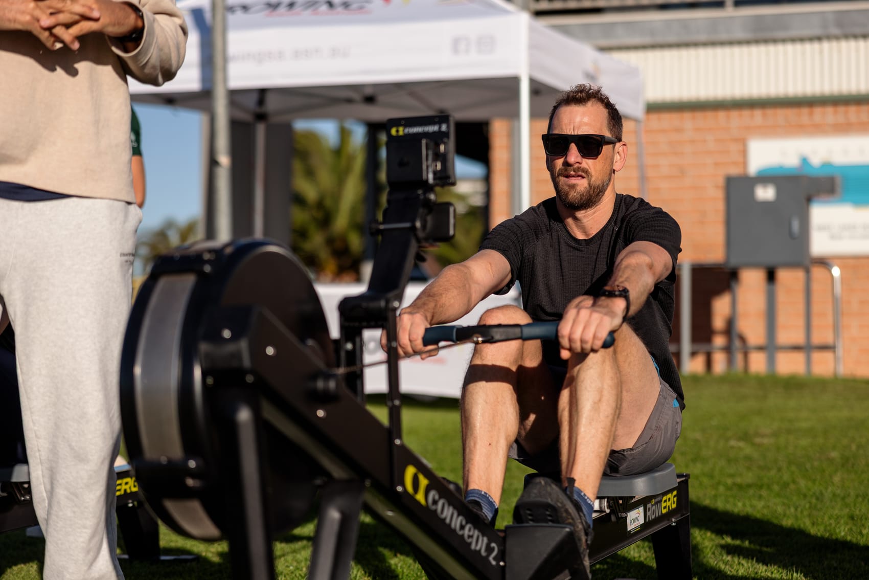 A mature athlete mid-stroke on a Concept2 RowErg outdoors, seated in the supported, low-impact rowing position